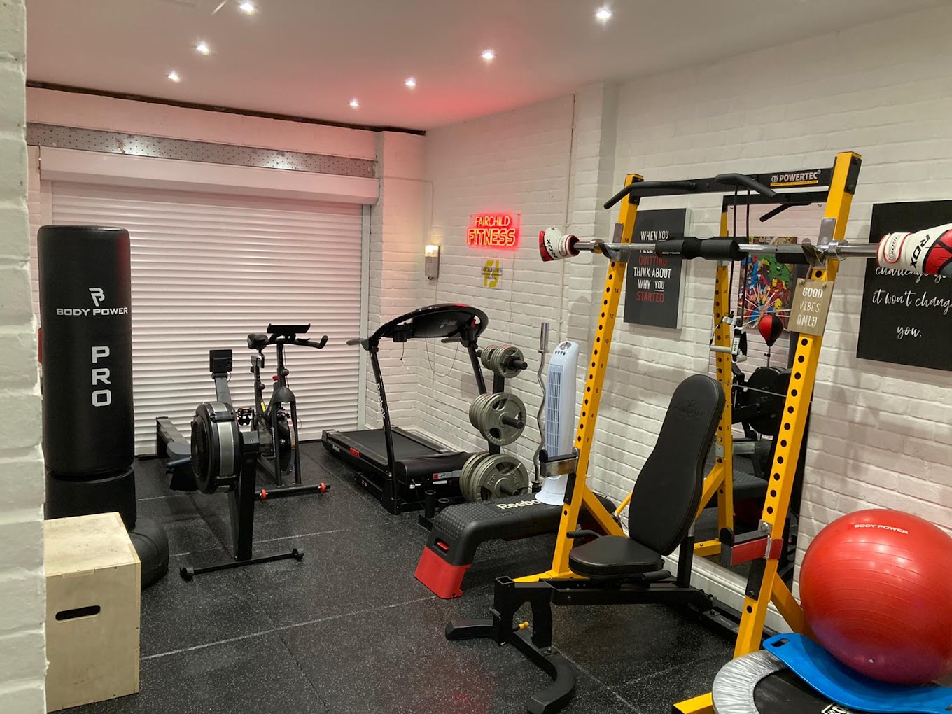 Fairchild Fitness's private gym in Black Notley, with the neon sign lit above a rower, spin bike, treadmill, and power rack