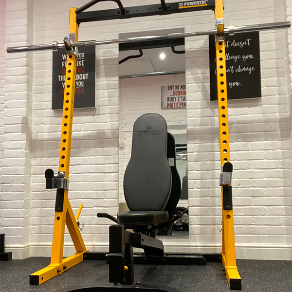 Power rack and mirror inside the Fairchild Fitness gym, with motivational posters on the white brick wall